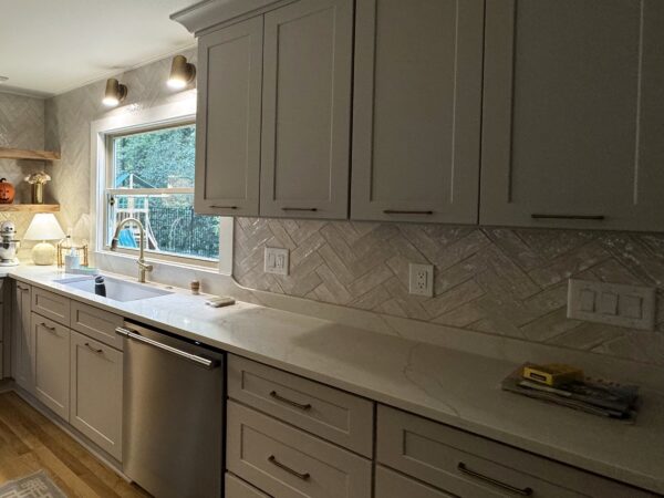 Glazed herringbone tile backsplash under gray shaker cabinets
