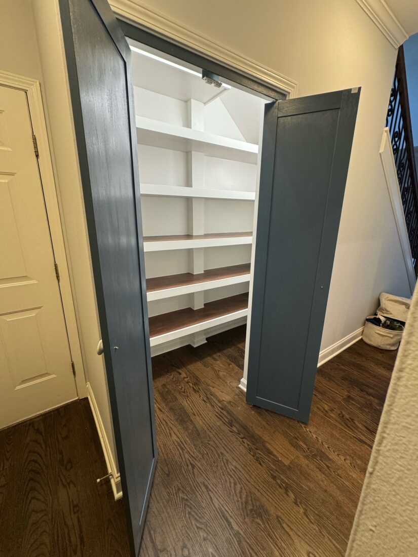 Walk-in pantry with doors open showing white shelving with stained wood tops