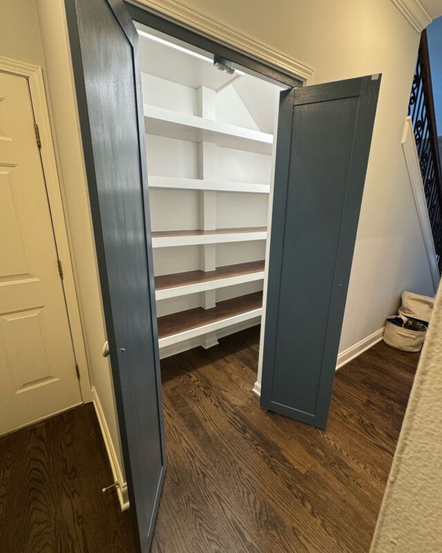 Walk-in pantry with doors open showing white shelving with stained wood tops