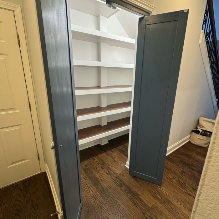 Walk-in pantry with doors open showing white shelving with stained wood tops