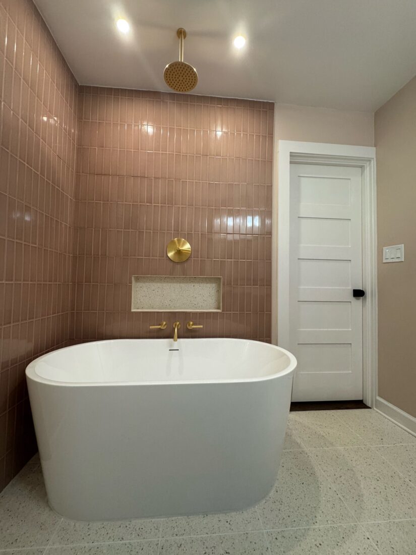 Full-height pink stacked tile tub and shower wall with brass rain shower and freestanding tub