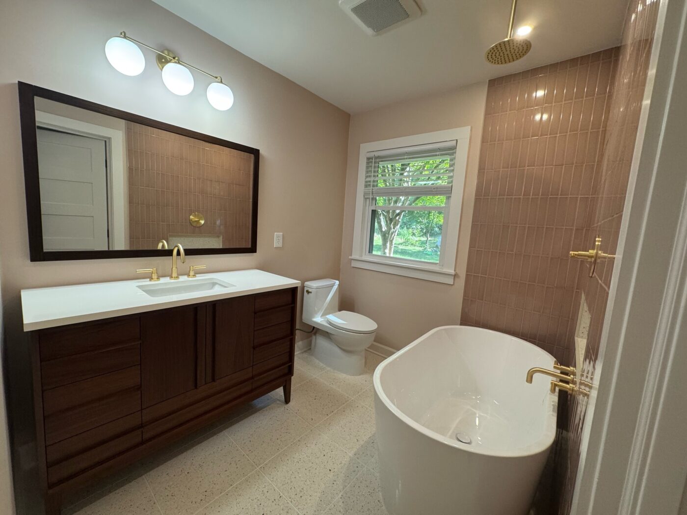 Renovated Roswell bathroom with walnut vanity, terrazzo tile floor, freestanding tub, and pink stacked tile shower wall